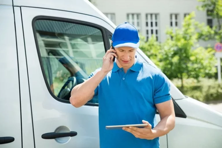 Un transporteur de colis devant son vehicule de transport avec une liste et un telephone en main