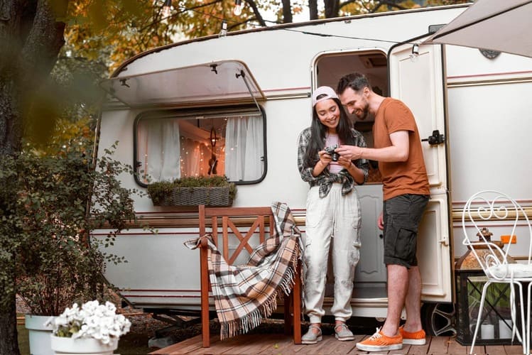 Un homme ce tien a cote dune femme tenante une camera devant un camping car